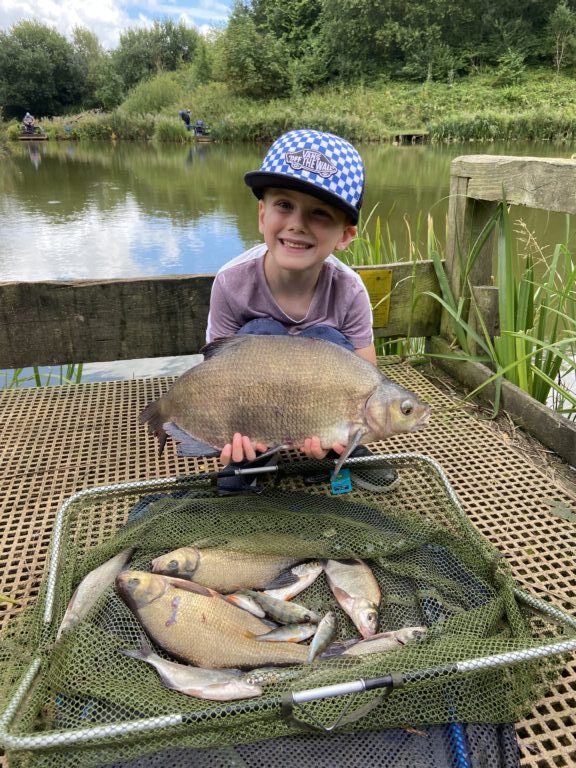 Picture of young boy wearing a blue cap. He is holding a fish and smiling proudly